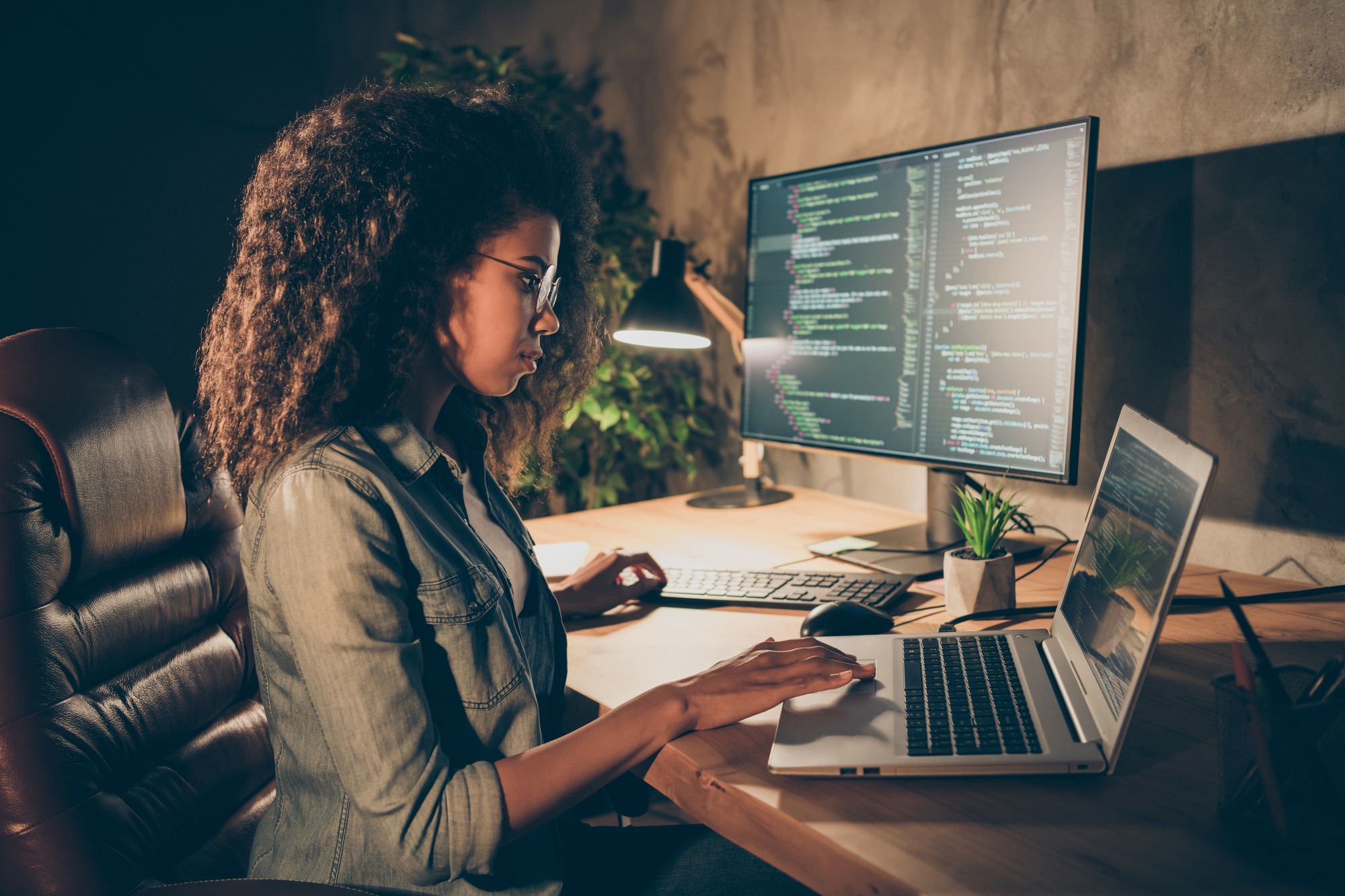 Profile Side Photo Focused Skilled Afro American Girl Web Designer Geek Freelancer Entrepreneur Sit Evening Table Work Computer Laptop Write Binary JavaScript Code in Workstation Workplace.