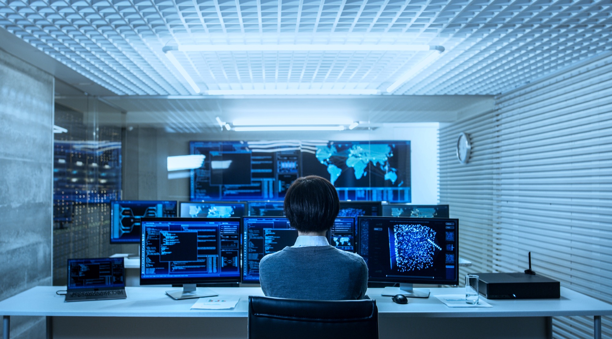 Back View of the It Engineer Working With Multiple Monitors Showing Graphics, Functional Neural Network. He Works in a Technologically Advanced System Control Data Center.